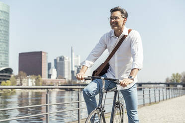 Lächelnder reifer Geschäftsmann stehend mit Fahrrad in der Stadt - UUF23167