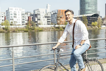 Mature male entrepreneur on bicycle by river on sunny day - UUF23169