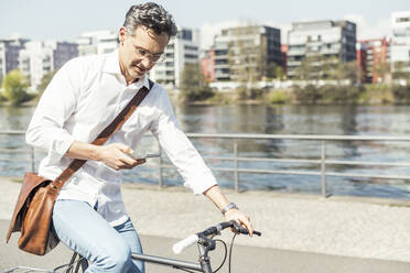 Businessman using mobile phone while cycling bicycle on sunny day - UUF23172