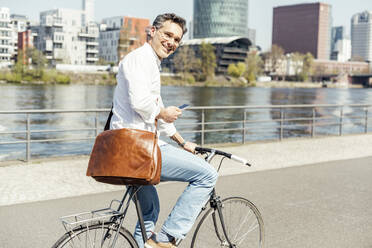 Lächelnder männlicher Unternehmer mit Mobiltelefon und Fahrrad auf dem Fußweg - UUF23173