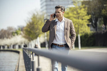 Male professional talking on mobile phone by railing - UUF23176