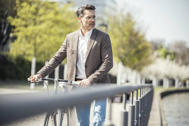 Thoughtful male entrepreneur with bicycle on sunny day - UUF23181