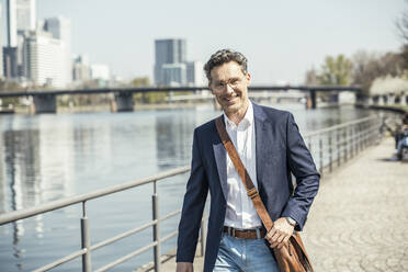 Male entrepreneur with crossbody bag standing on footpath - UUF23191