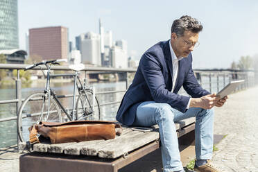 Male entrepreneur using digital tablet while sitting on bench - UUF23202