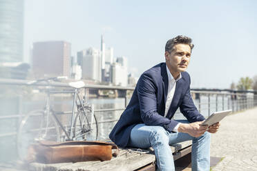 Male entrepreneur with digital tablet sitting on bench during sunny day - UUF23204