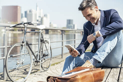 Businessman smiling at video call through mobile phone while sitting on bench - UUF23213