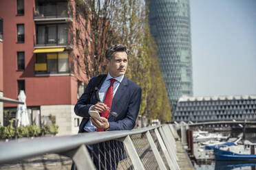 Thoughtful businessman leaning on railing during sunny day - UUF23218