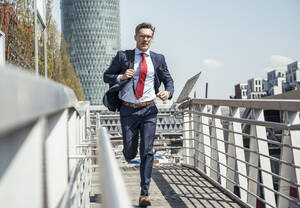 Businessman with backpack running on footpath - UUF23230