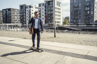 Businessman talking on mobile phone while skateboarding in city - UUF23233