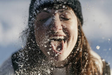 Mittlere erwachsene Frau streckt beim Spielen im Schnee die Zunge heraus - MJRF00491