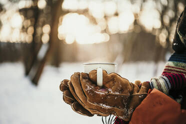 Frau mit Handschuhen hält Becher im Wald - MJRF00495