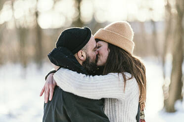 Mid adult couple in warm clothing kissing each other in forest - MJRF00496