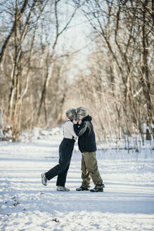 Mid adult couple kissing each other while standing on snow path in forest - MJRF00500