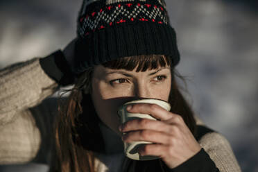 Frau mit Strickmütze schaut beim Kaffeetrinken weg - MJRF00504