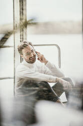 Lächelnder Mann, der in einem Hausboot mit seinem Handy telefoniert - MJRF00531