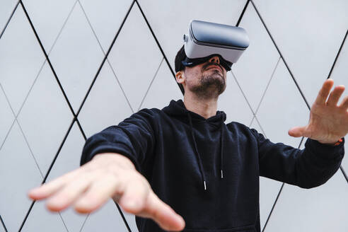 Mann trägt Virtual-Reality-Headset und gestikuliert in der Nähe einer Wand - ASGF00290