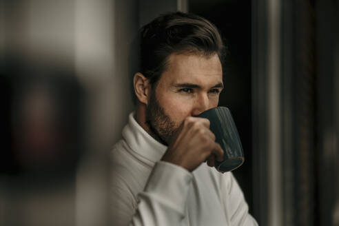 Mann trinkt Kaffee, während er zu Hause wegschaut - MJRF00547