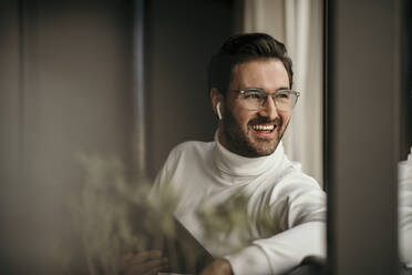 Cheerful businessman holding digital tablet while looking through window at home - MJRF00567