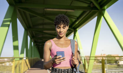 Woman using smart phone at bridge during sunny day - JCCMF02489