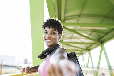 Lächelnde junge Frau mit Kopfhörern auf einer Brücke - JCCMF02494