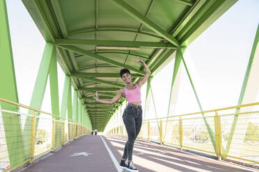 Lächelnde junge Frau, die auf einer Brücke stehend ein Friedenszeichen macht - JCCMF02498