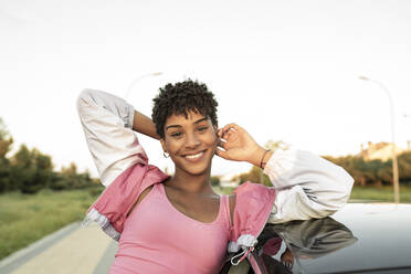 Smiling woman with head in hands near car - JCCMF02545