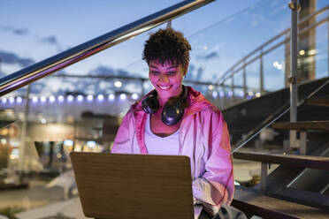 Young woman using laptop while sitting on steps during night - JCCMF02555