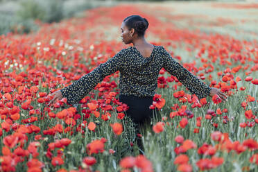 Mittlere erwachsene Frau, die Blumen in einem Mohnfeld berührt - JRVF00626