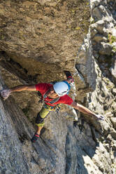 Mature man looking up while climbing on rock mountain - JMPF00959