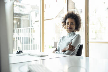 Female entrepreneur with arms crossed sitting at desk - UUF23255