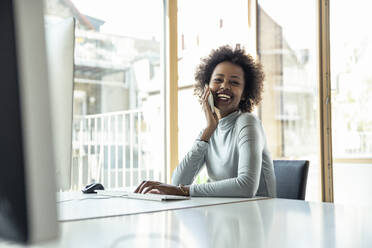 Smiling businesswoman talking on mobile phone at desk - UUF23257