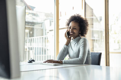 Eine fröhliche Frau im Büro, die mit professionellem Auftreten über ihr Smartphone plaudert - UUF23258