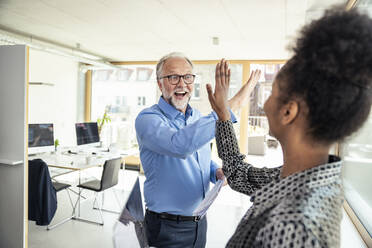 Zwei Kollegen feiern ihren Erfolg mit einem High-Five und verbreiten so positive Stimmung und Teamwork im Büro - UUF23279