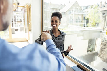 Smiling female professional doing fist bump with male colleague in office - UUF23281