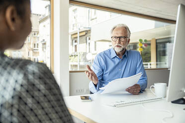 Businessman with documents explaining strategy with female colleague at desk - UUF23283