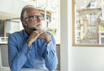 Businessman wearing eyeglasses while contemplating at desk - UUF23290