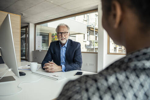 Zwei Kollegen, ein Mann und eine Frau, unterhalten sich in einem professionellen Büro mit verschränkten Händen - UUF23291