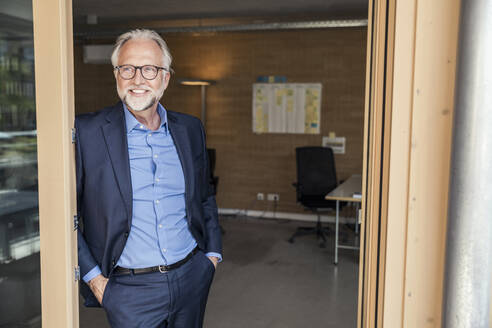 Businessman with hands in pockets leaning on doorframe at office - UUF23295