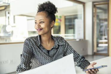 Eine erfolgreiche Geschäftsfrau strahlt Zuversicht und Freude aus, während sie an ihrem Schreibtisch in einer professionellen Büroumgebung sitzt - UUF23298