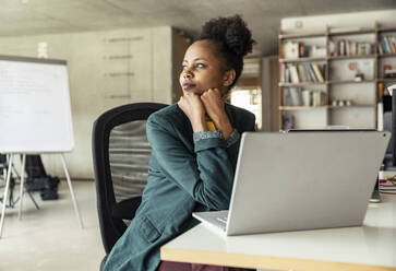 Female entrepreneur with hand on chin day dreaming at desk - UUF23316