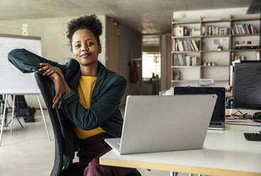 Eine konzentrierte Geschäftsfrau arbeitet an ihrem Laptop, während sie bequem auf einem Stuhl an ihrem Schreibtisch sitzt - UUF23318