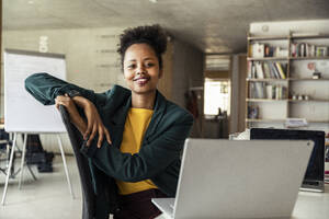 Smiling female professional sitting on chair at desk - UUF23319