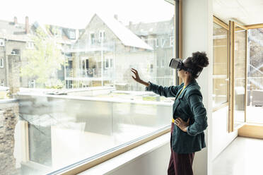 Businesswoman with hand on hip using wearable computer while touching glass at office - UUF23322