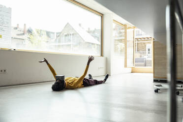 Female professional wearing virtual reality simulator while lying on floor at office - UUF23331