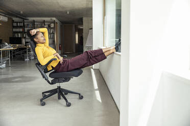 Eine erfolgreiche Geschäftsfrau macht eine wohlverdiente Pause, legt die Füße hoch und entspannt sich in ihrem Bürostuhl - UUF23333