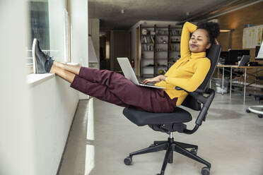 Eine erfolgreiche Geschäftsfrau nimmt sich einen Moment Zeit, um sich mit ihrem Laptop in ihrer komfortablen Bürowohnung zu entspannen - UUF23336