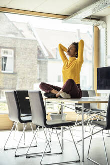 Businesswoman with arms raised meditating on desk at office - UUF23346