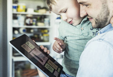 Lächelnder erwachsener Mann mit Sohn, der in der Küche auf ein digitales Tablet zeigt - UUF23354