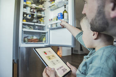 Junge mit Vater, der ein Tablet hält und auf den Kühlschrank in der Küche zeigt - UUF23355