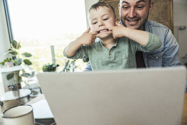 Junge neckt, während er mit seinem Vater sitzt und einen Videoanruf über den Laptop zu Hause führt - UUF23395